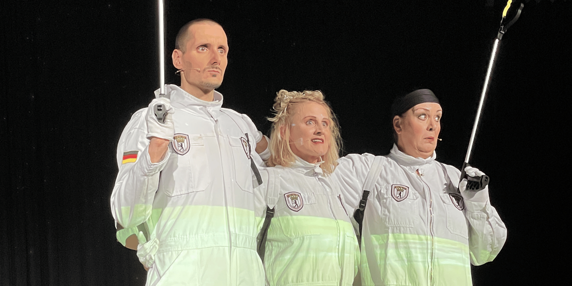 2 Frauen und 1 Mann stehend mit weißen Anzügen auf einer Bühne