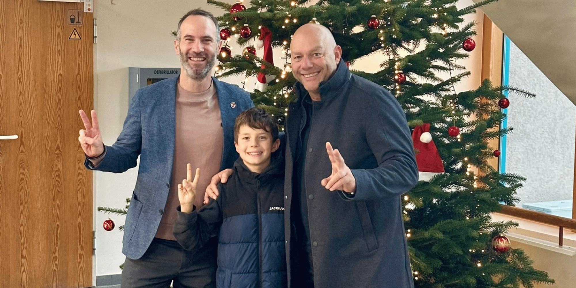 Zwei Männer und ein Junge vor einem dekorierten Weihnachtsbaum im Foyer des Rathauses