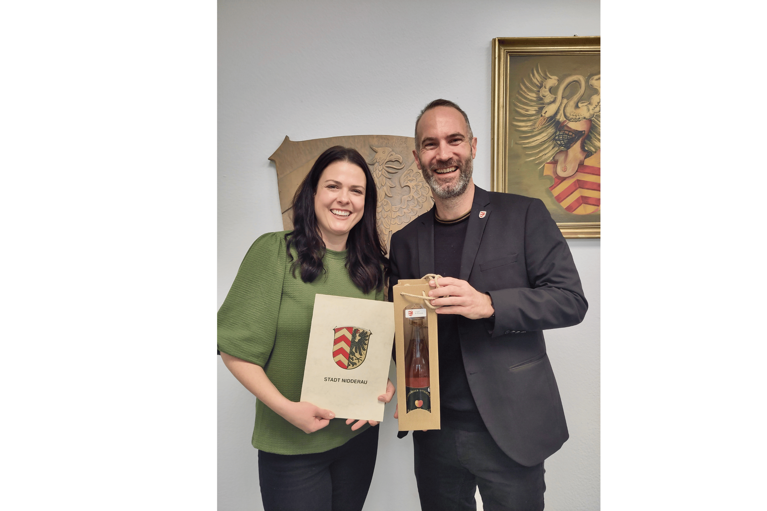 Frau im grünen Pullover hält eine Urkunde neben einem Mann im Anzug