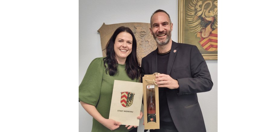 Frau im grünen Pullover hält eine Urkunde neben einem Mann im Anzug