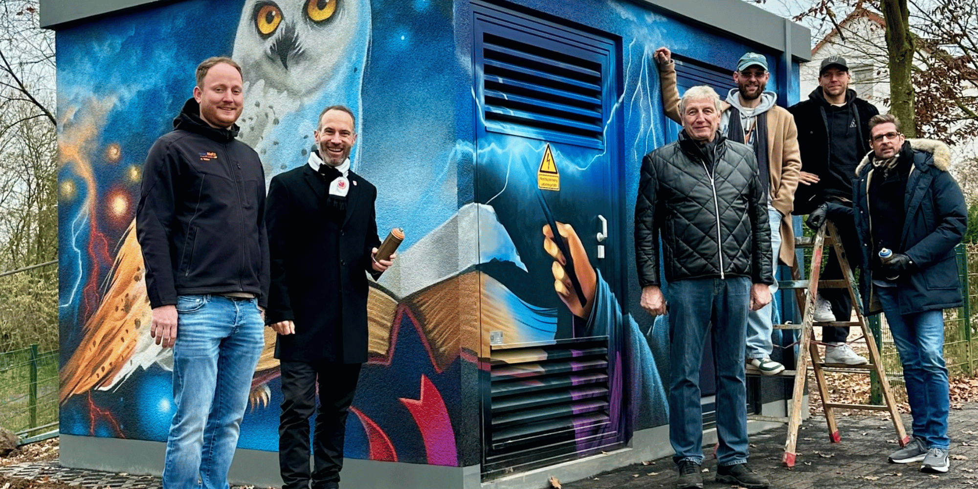 Mehrere Männer stehend vor einer Trafostation, welche mit einem Graffiti verschönert wurde