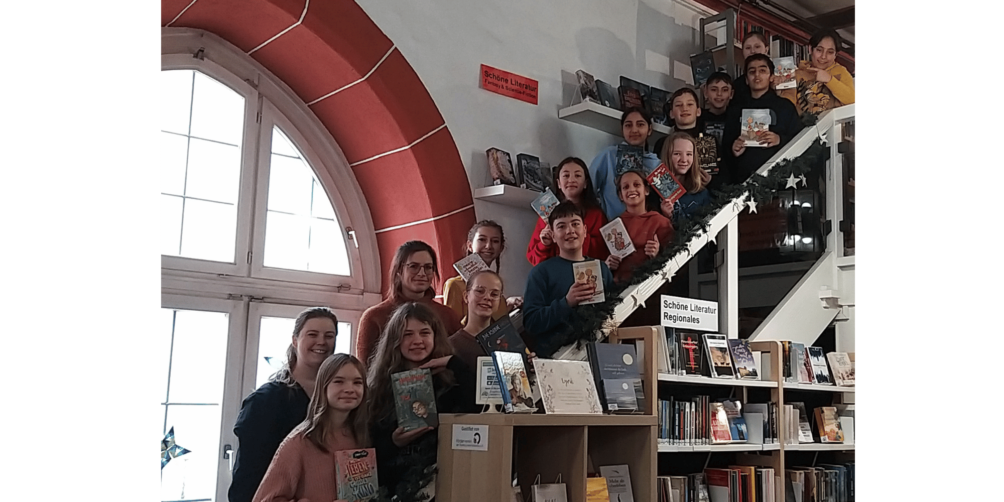 Mehrere Kinder auf einer Treppe stehend hinter einem großen Bürcherregal
