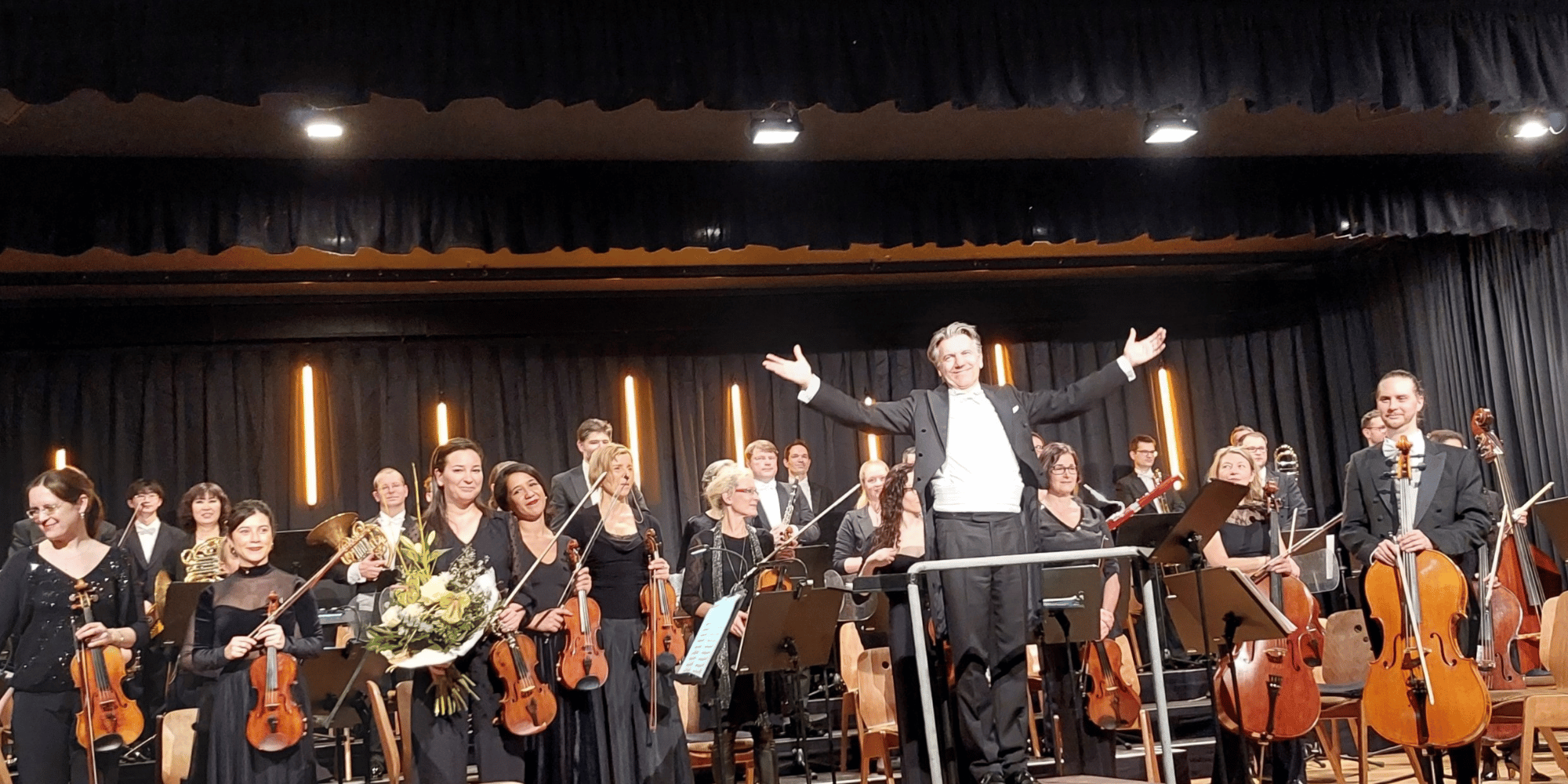 Mehrere Personen in schwarz gekleidet auf einer Bühne mit Musikinstrumenten