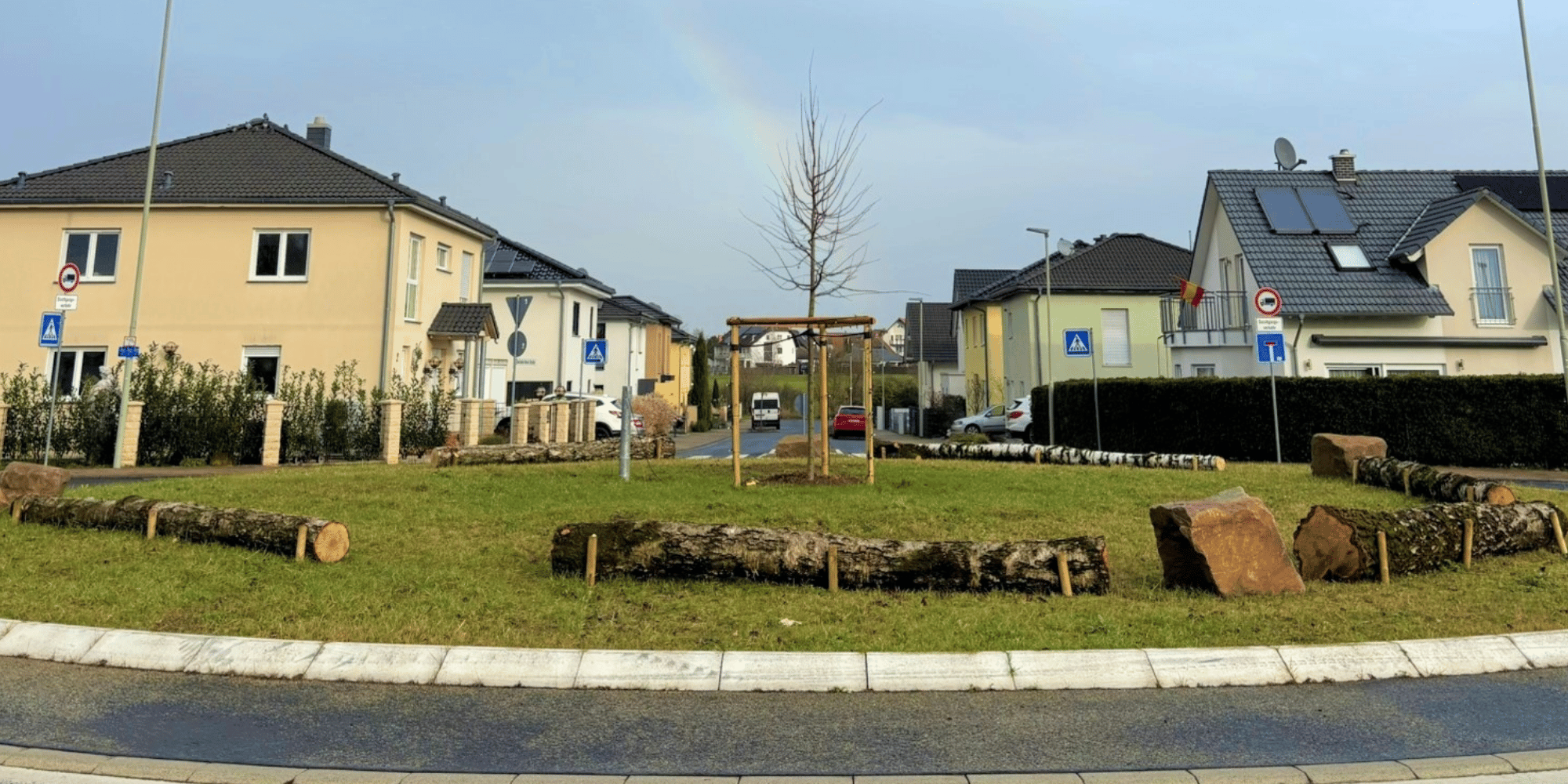 Verkehrskreisel mit liegenden fixierten Baumstämmen und einem gepflanzten Baum in der Mitte des Kreisels