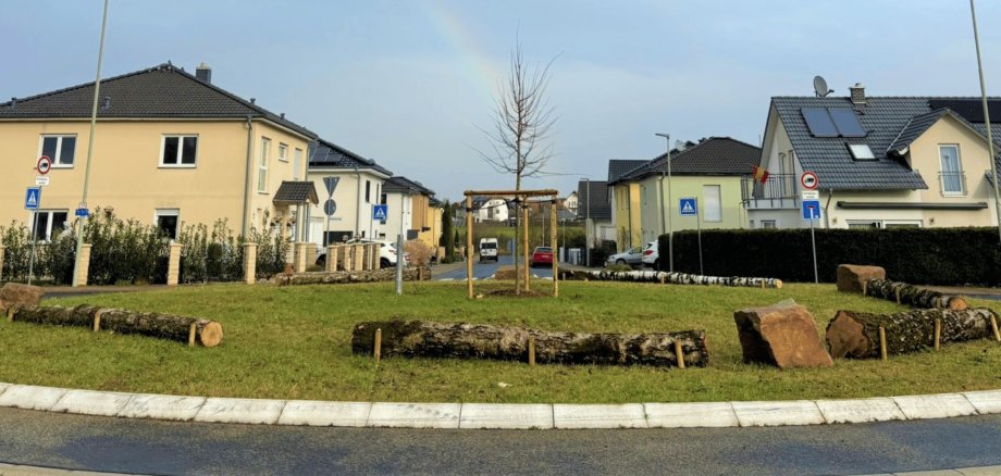 Verkehrskreisel mit liegenden fixierten Baumstämmen und einem gepflanzten Baum in der Mitte des Kreisels