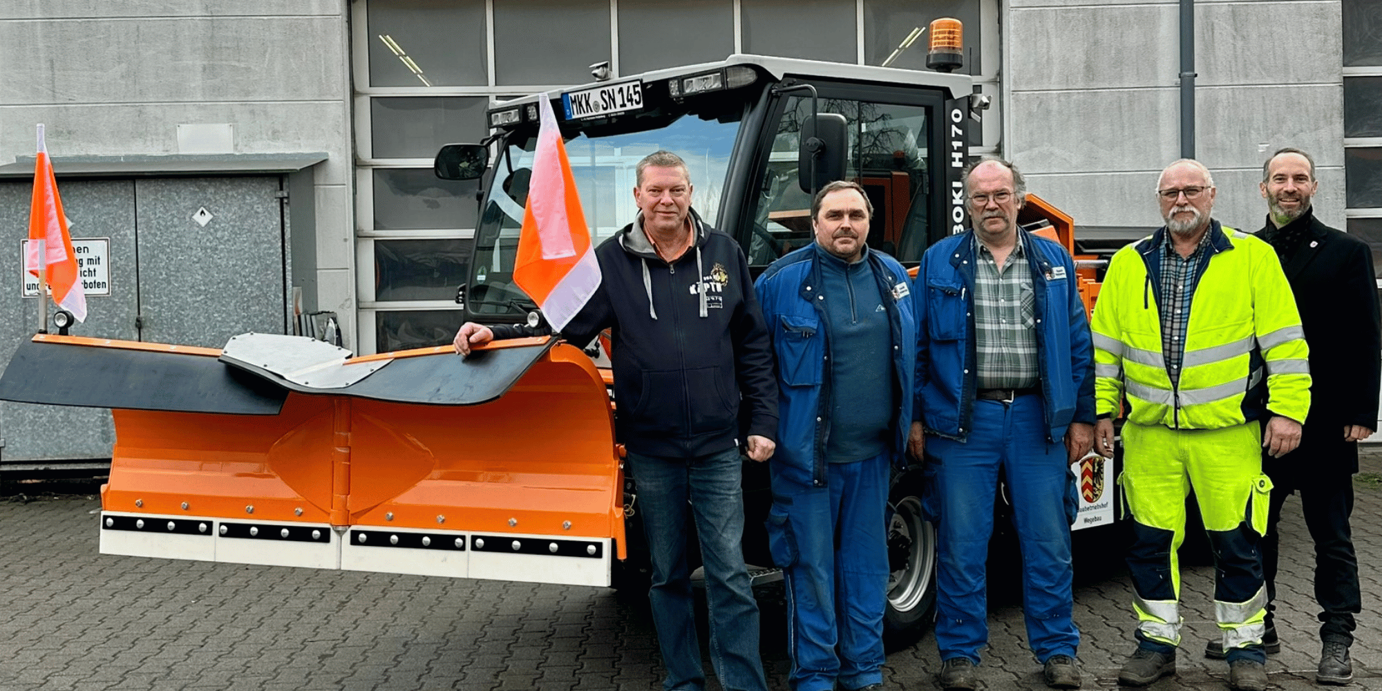 Schneeräumfahrzeug, davor 5 Männer stehend