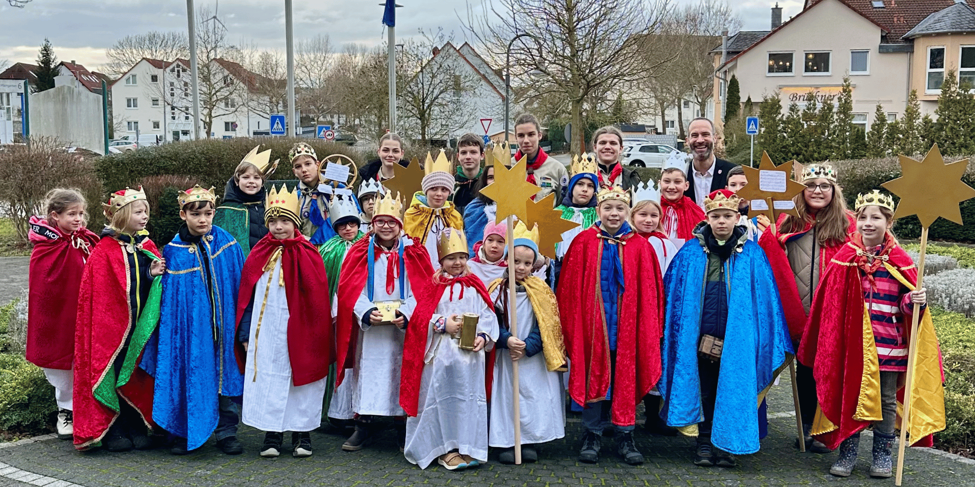 Kinder mit bunten Gewändern und selbstgebastelten Kronen stehen zusammen vor dem Rathaus