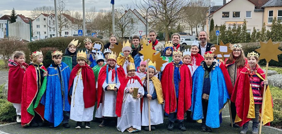 Kinder mit bunten Gewändern und selbstgebastelten Kronen stehen zusammen vor dem Rathaus