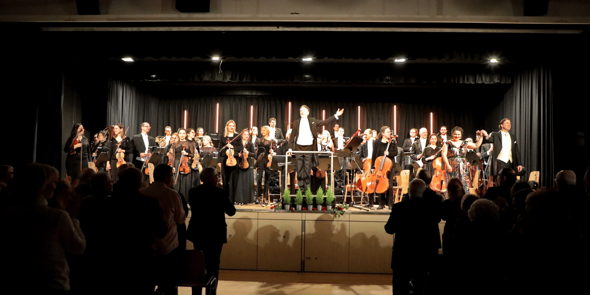 Mehrere Musiker mit Instrumenten auf einer schwarzen Bühne. Davor Publikum