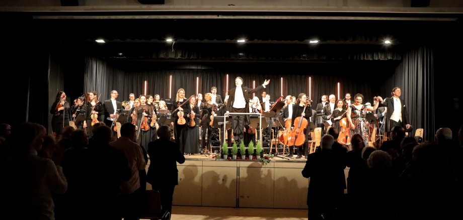 Mehrere Musiker mit Instrumenten auf einer schwarzen Bühne. Davor Publikum