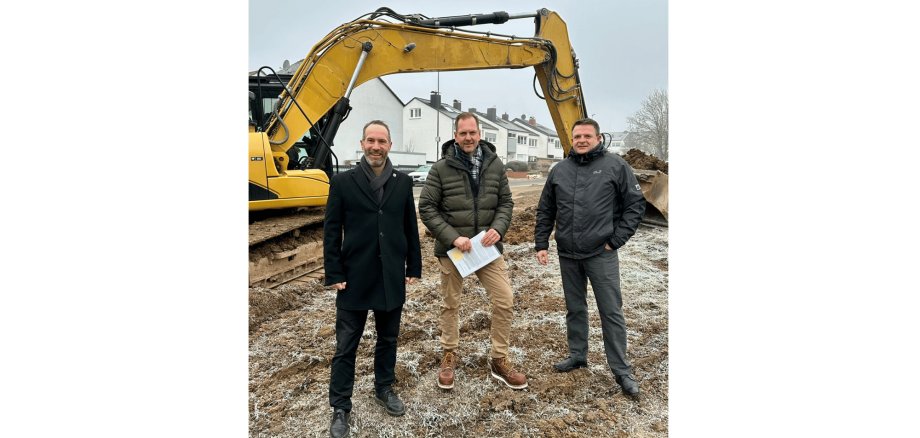 3 Männer stehend vor einem Bagger