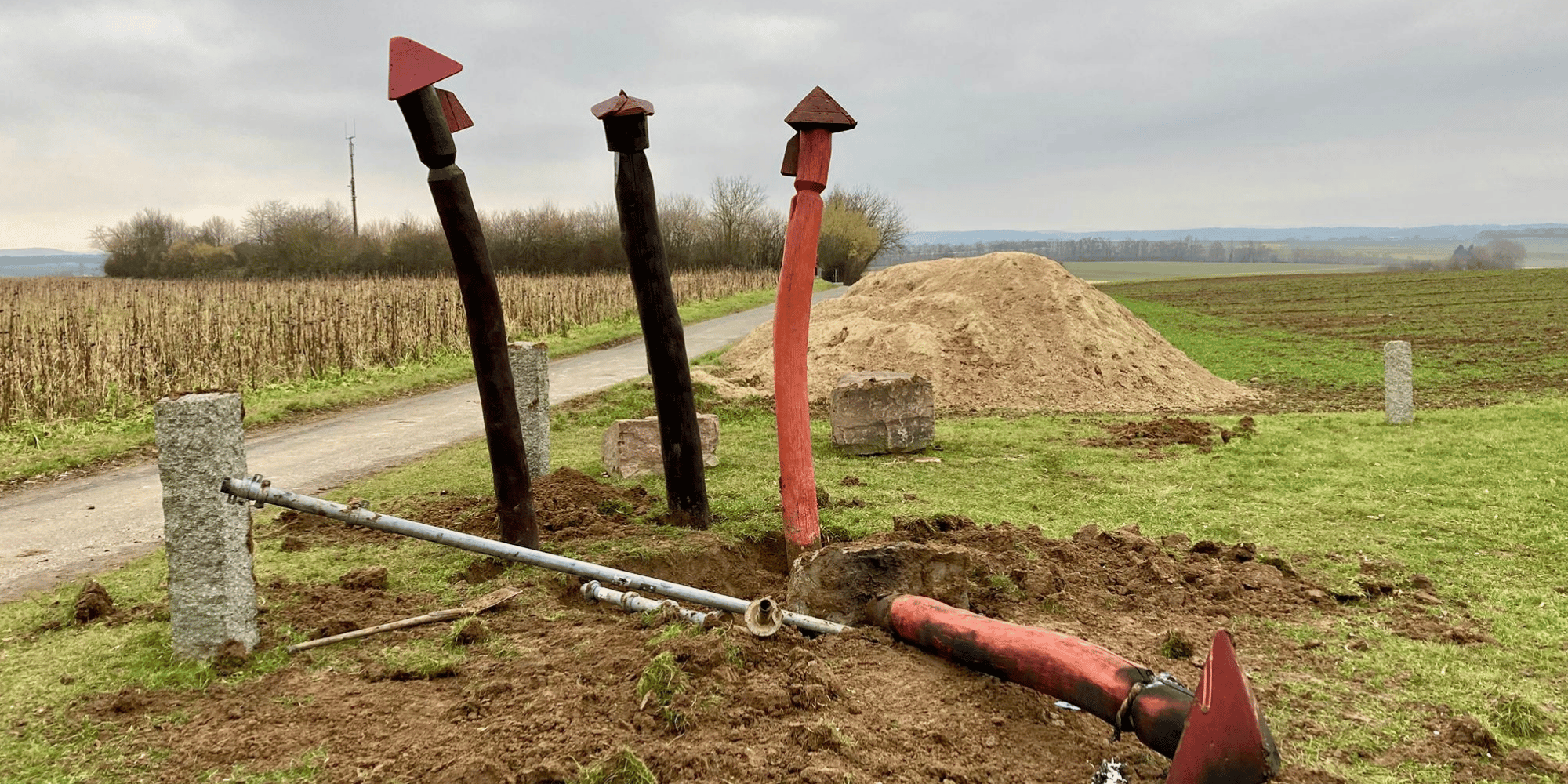 Vier Holzpfähle auf einem Feld, einer liegt am Boden