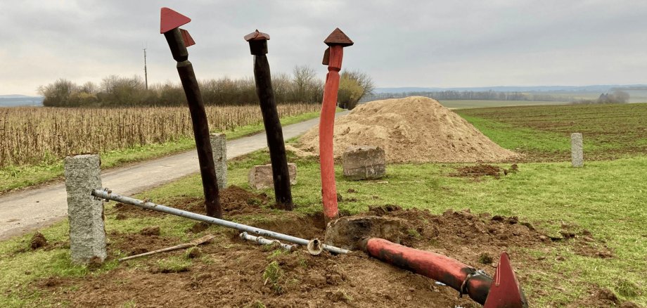 Vier Holzpfähle auf einem Feld, einer liegt am Boden