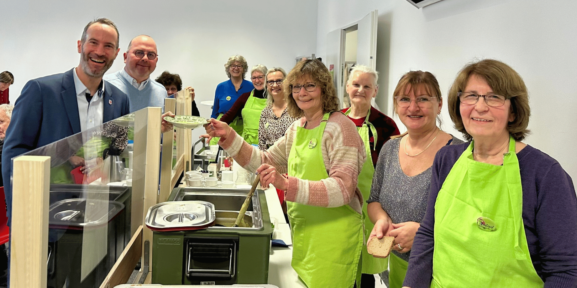 Suppenausgabe mit Frauen in grünen Schürzen