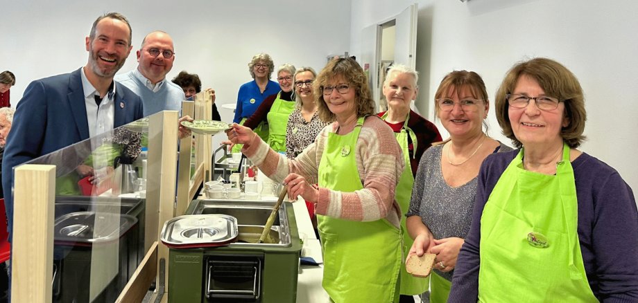 Suppenausgabe mit Frauen in grünen Schürzen