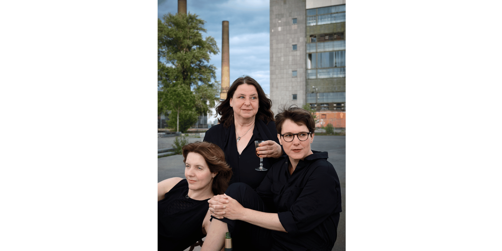 3 Frauen in schwarzer Kleidung mit vor einem Betonbau