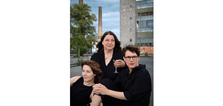 3 Frauen in schwarzer Kleidung mit vor einem Betonbau