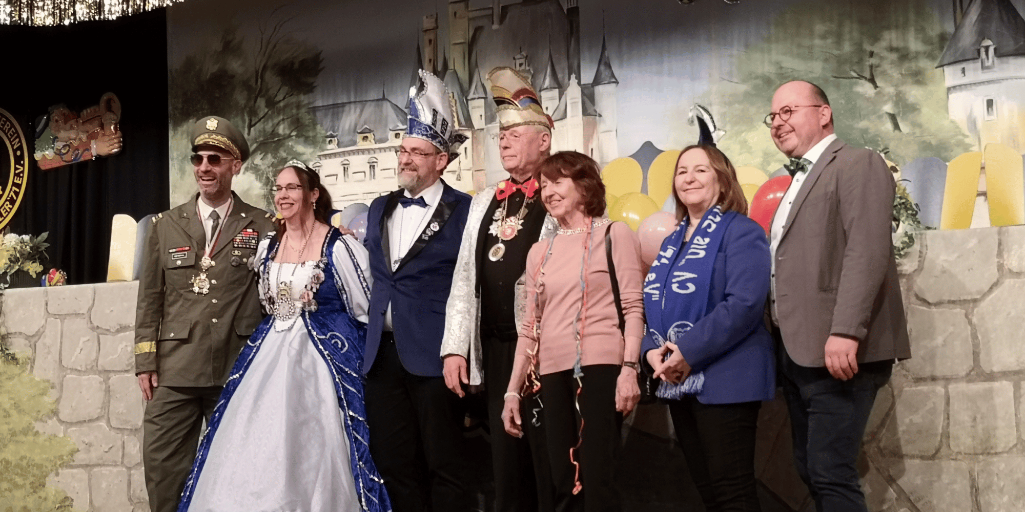 Sieben erwachsene Personen in Faschingskleidung stehend auf einer Bühne