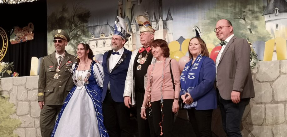 Sieben erwachsene Personen in Faschingskleidung stehend auf einer Bühne