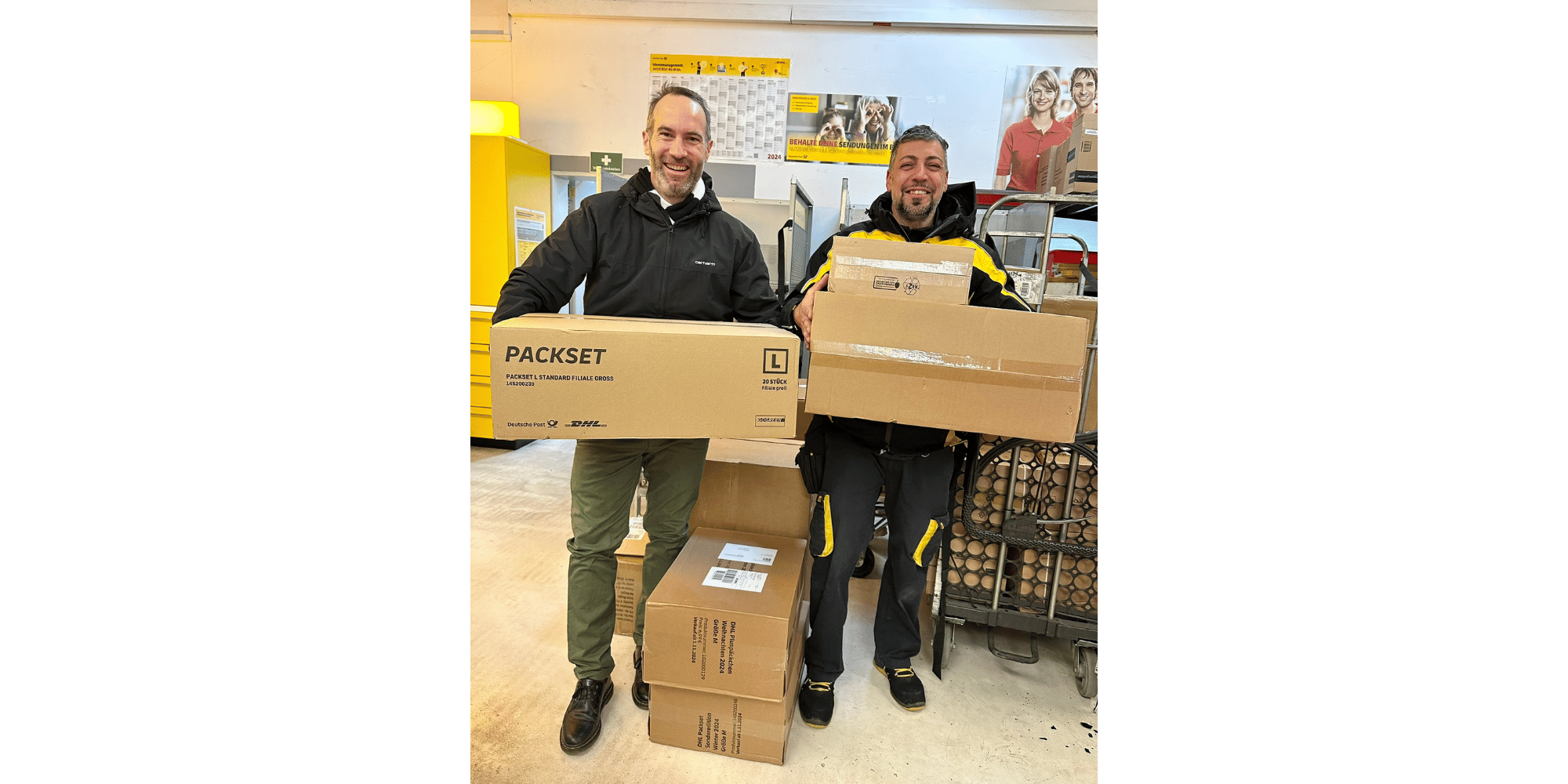 Zwei Männer stehend und Pakete haltend in einem Zustellstützpunkt der Post