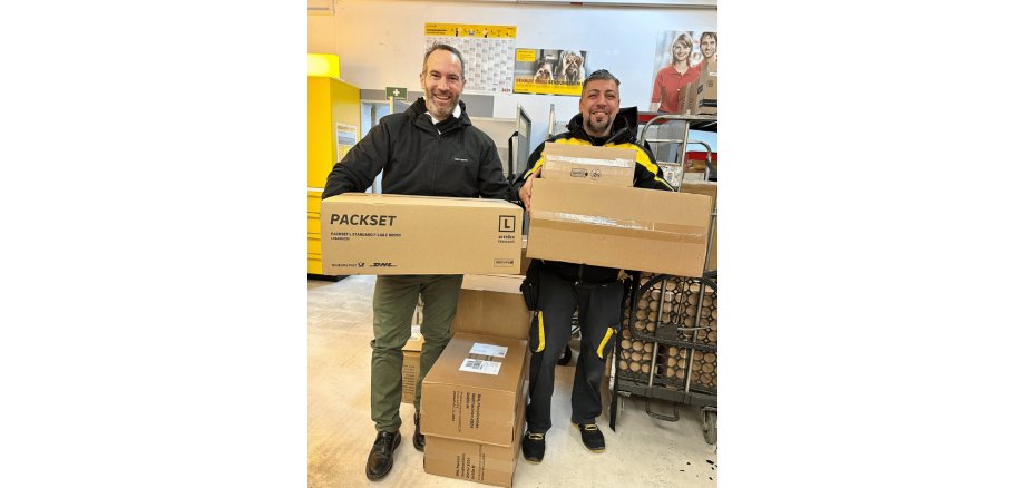 Zwei Männer stehend und Pakete haltend in einem Zustellstützpunkt der Post