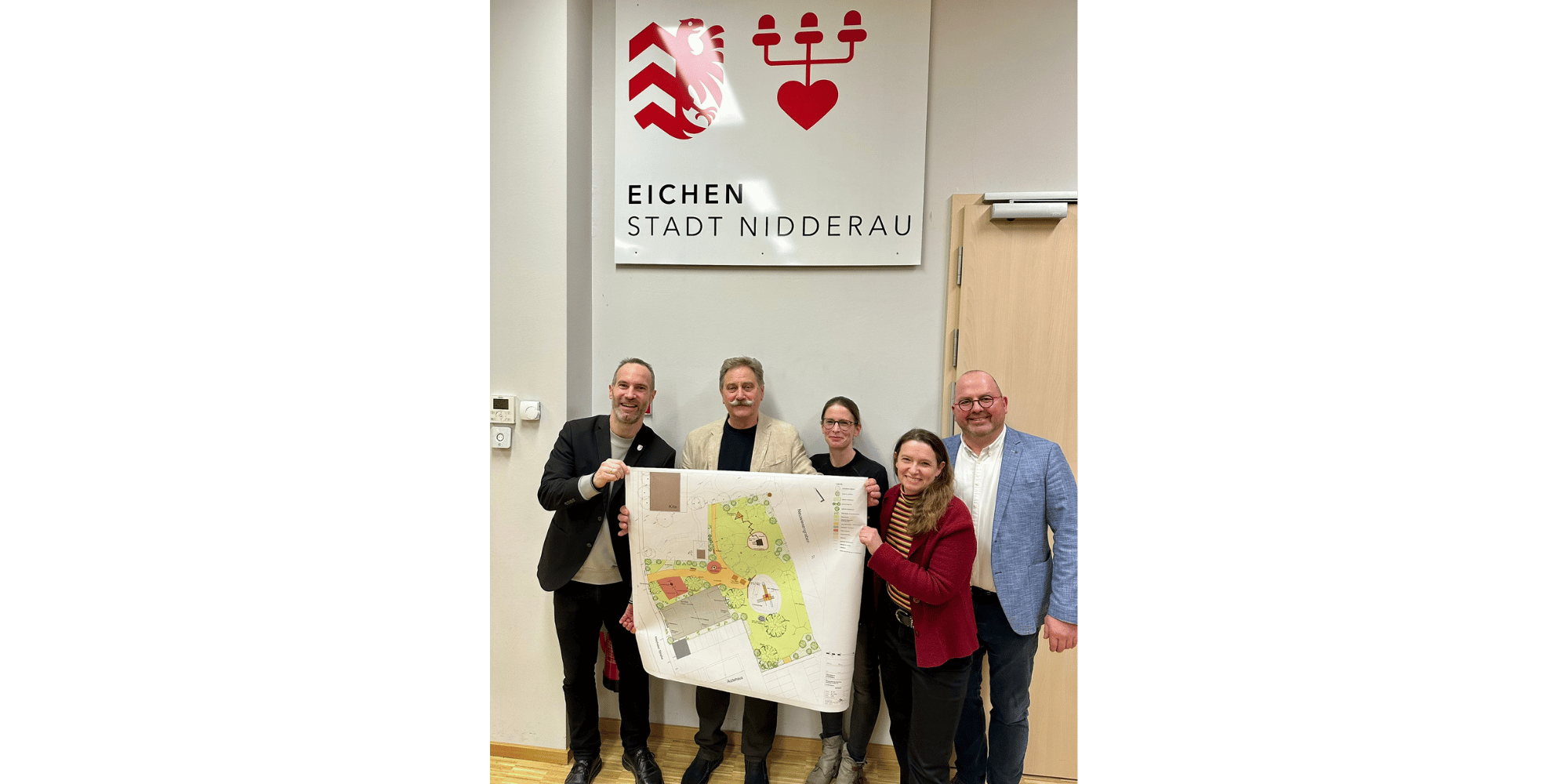 3 Männer und 2 Frauen stehend unter dem Stadtteilwappen von Eichen und einen Plan haltend