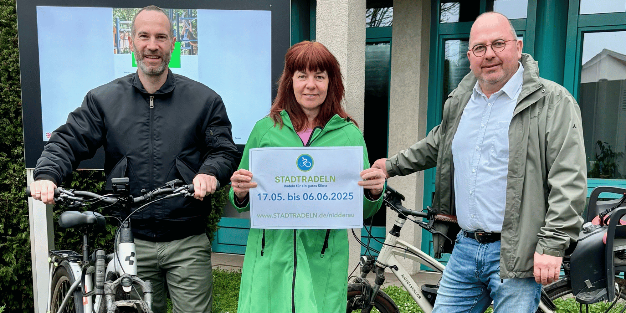 Zwei Männer und eine Frau stehend mit 2 Fahrrädern vor einem Display