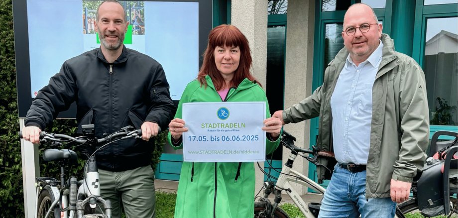 Zwei Männer und eine Frau stehend mit 2 Fahrrädern vor einem Display