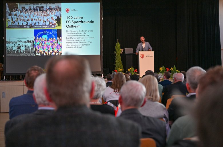 Bühne mit Leinwand darauf, Rednerpult und einem Mann stehend