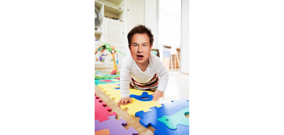 Baby krabbelt auf dem Boden. Das Baby hat einen Männerkopf