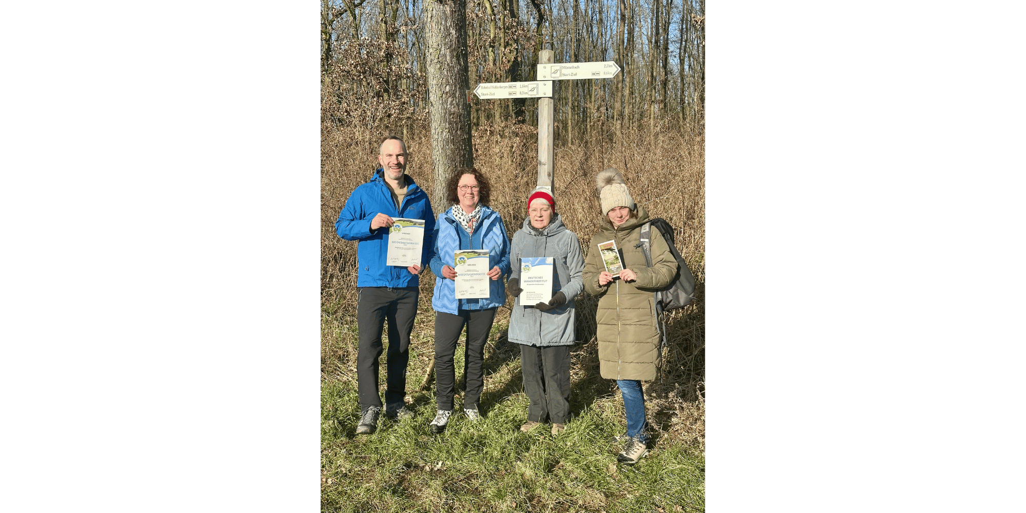 Ein Mann und drei Frauen stehend vor einem Wegweiser am Waldrand