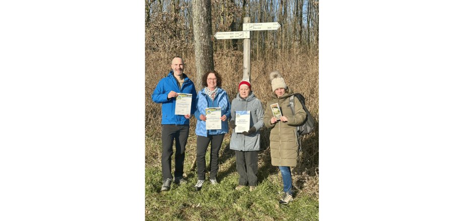 Ein Mann und drei Frauen stehend vor einem Wegweiser am Waldrand