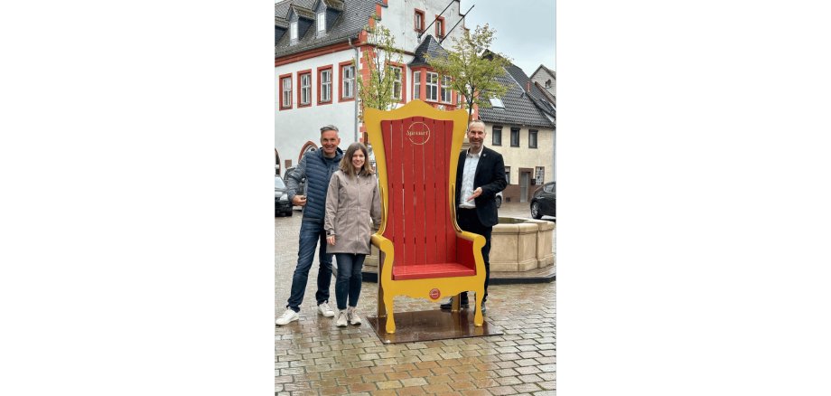 Zwei Männer und eine Frau stehend neben einem großen Thron aus Holz