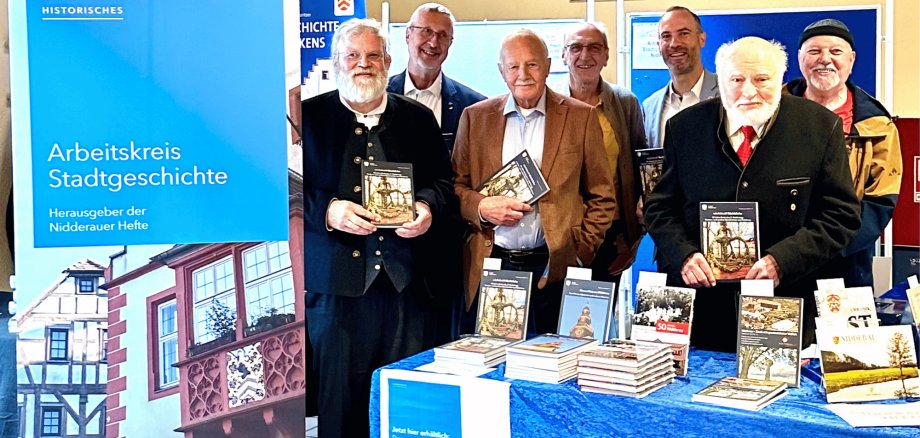 Mehrere ältere Männer stehend vor einem Verkaufsstand mit Büchern