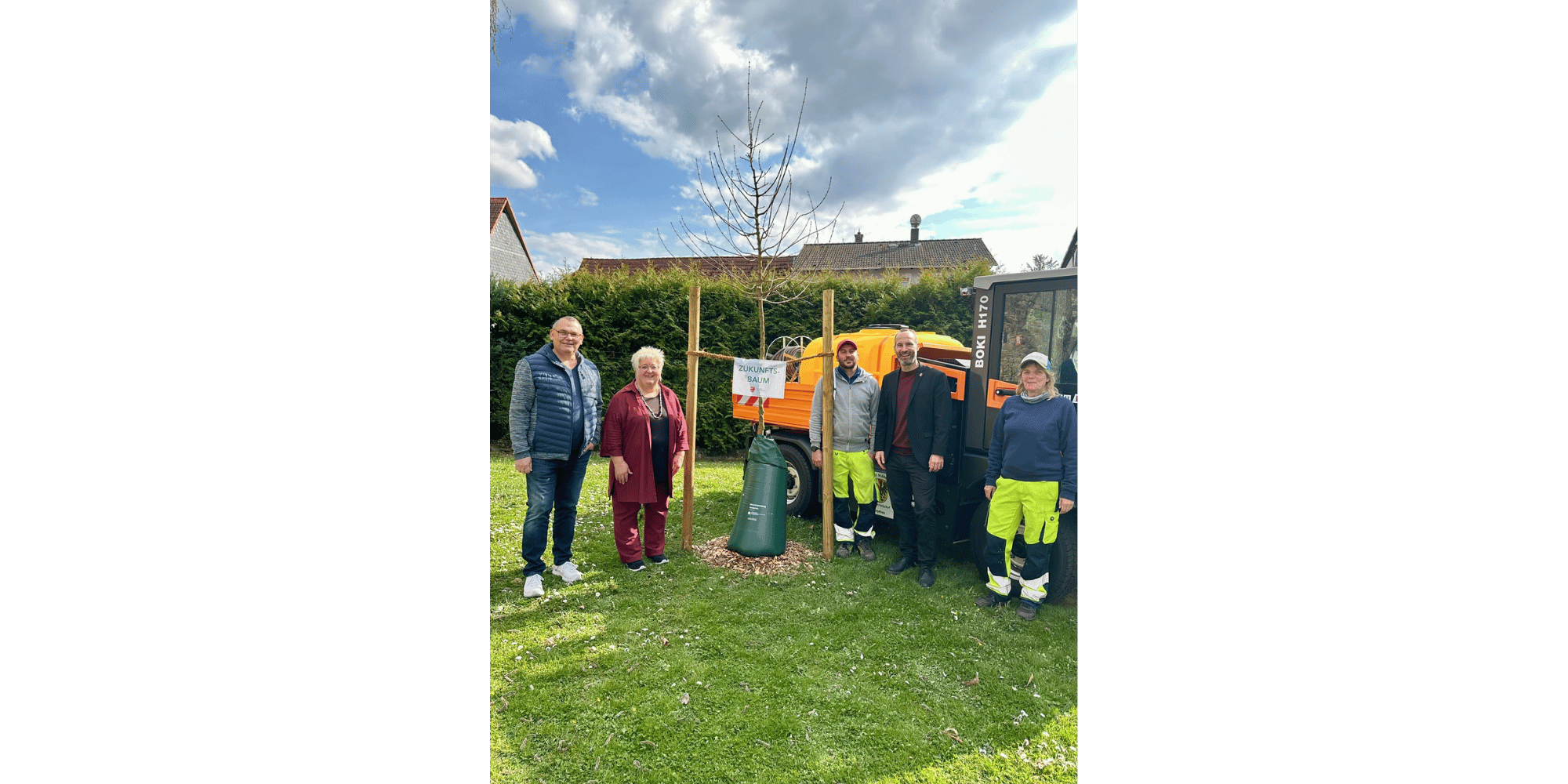 Drei Männer und zwei Frauen stehend neben einem gepflanzten Baum