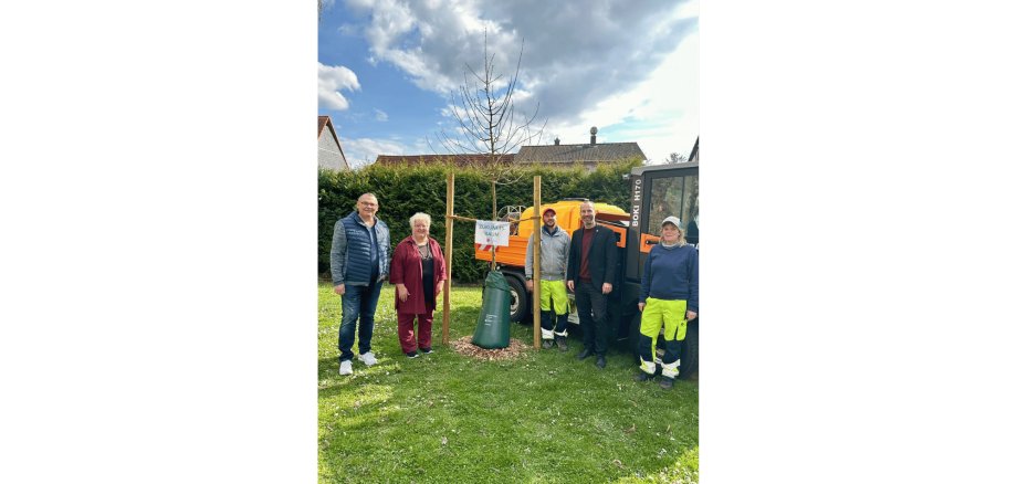 Drei Männer und zwei Frauen stehend neben einem gepflanzten Baum