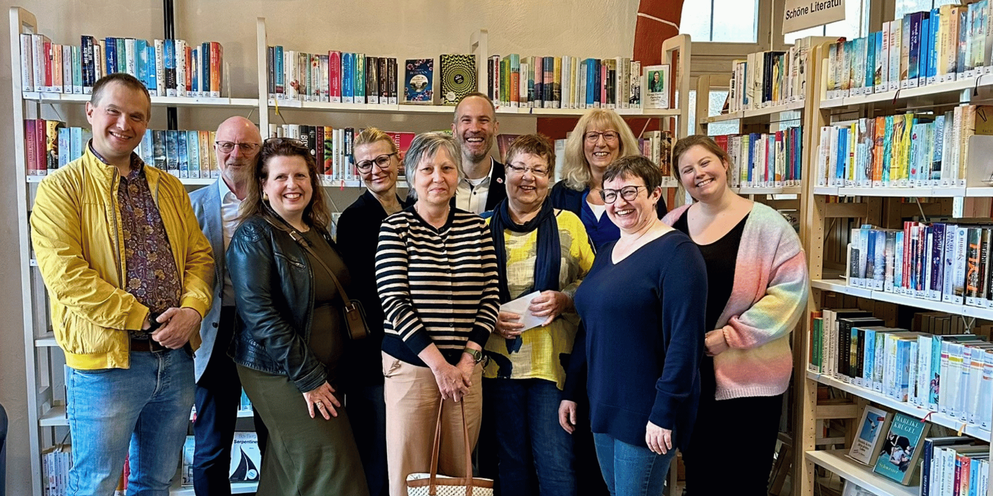 Mehrere Menschen zusammen stehend vor Bücherregalen in einer Bücherei