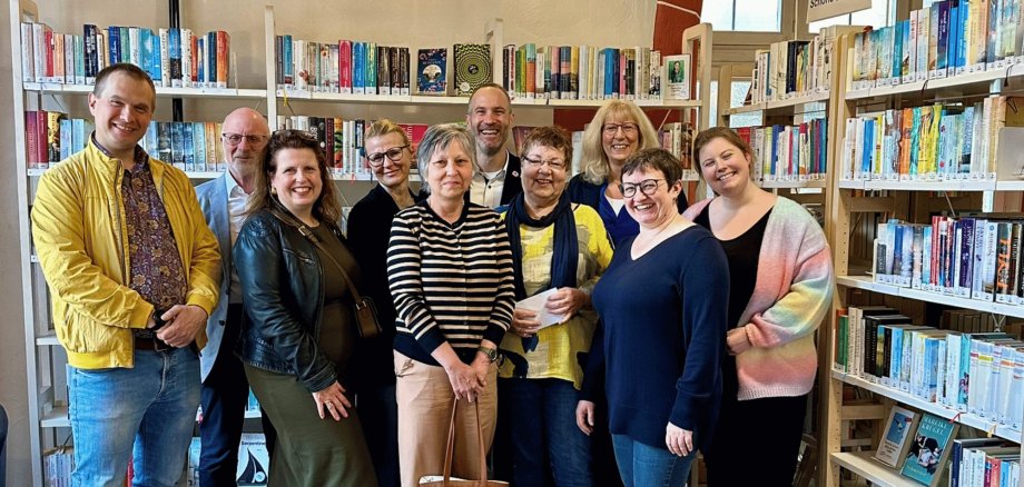Mehrere Menschen zusammen stehend vor Bücherregalen in einer Bücherei