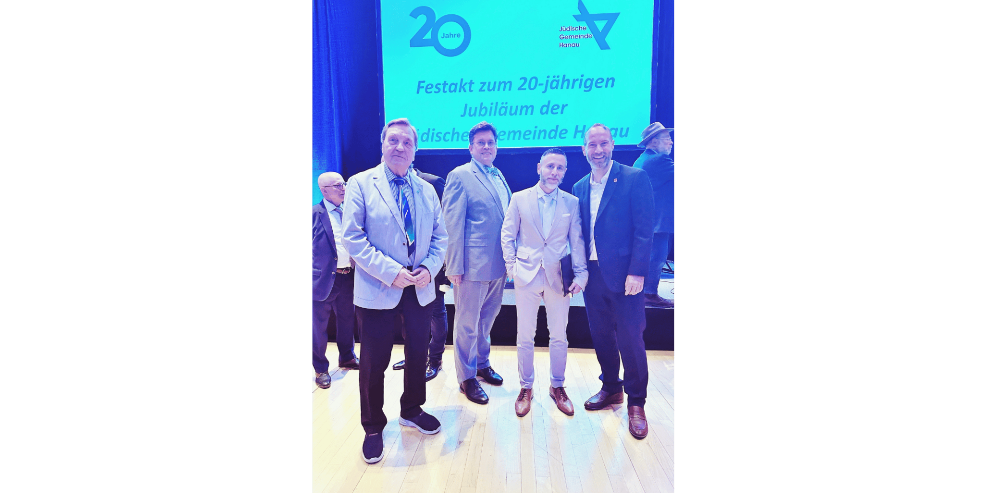 4 Männer in hellen Anzügen stehend vor einer Leinwand