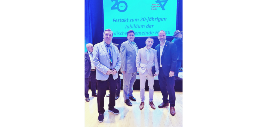 4 Männer in hellen Anzügen stehend vor einer Leinwand