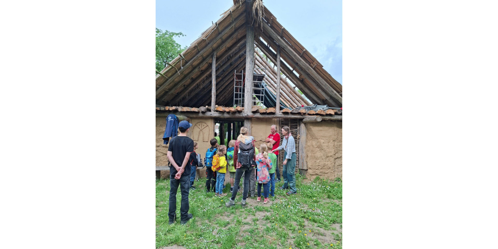 Kinder vor einem nachgebauten Haus aus Lehm und Holz