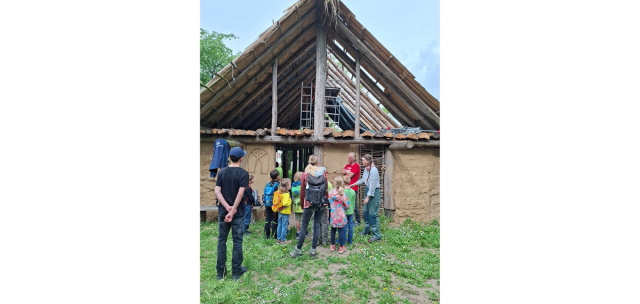 Kinder vor einem nachgebauten Haus aus Lehm und Holz