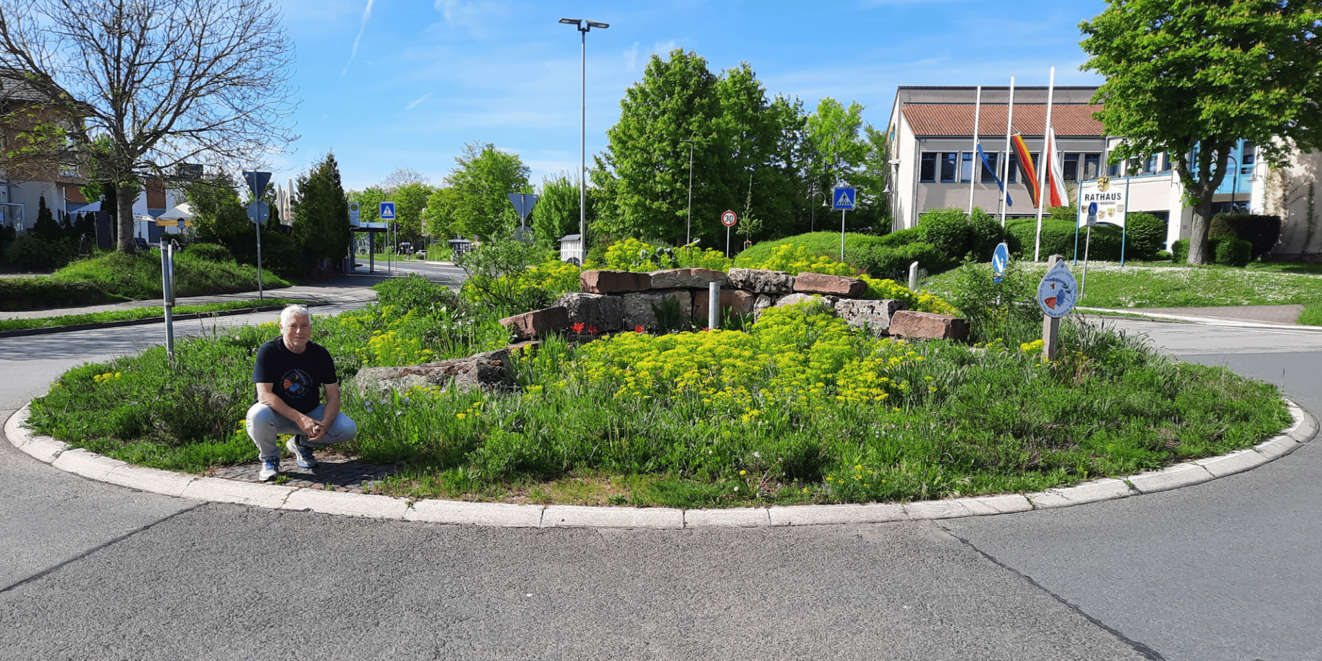 Ein Mann hockend vor einem bepflanzten Verkehrskreisel