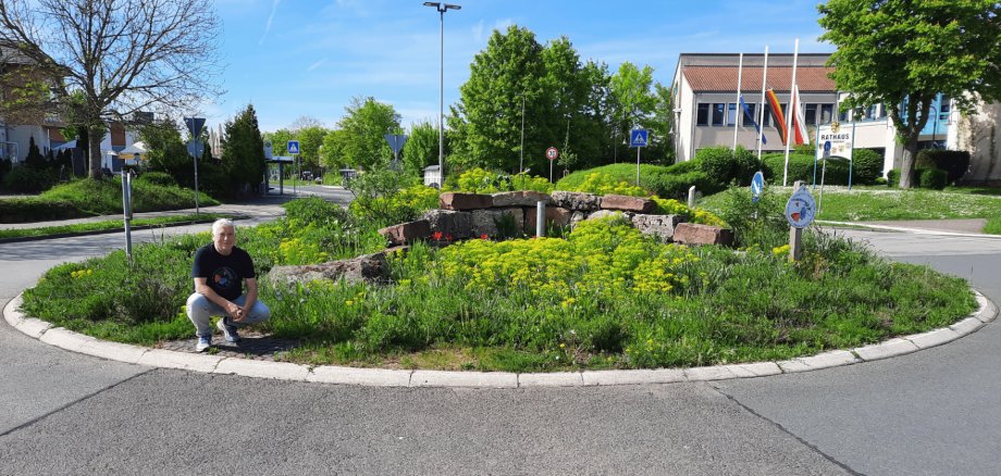 Ein Mann hockend vor einem bepflanzten Verkehrskreisel