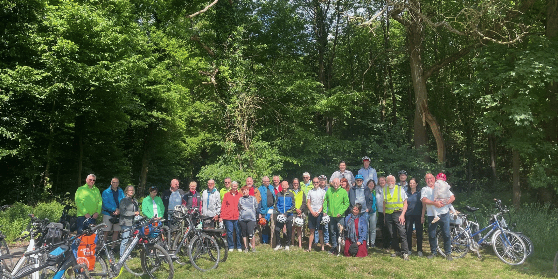 Mehrere Leute vor einem Wald stehend, links und rechts davon abgestellte Fahrräder