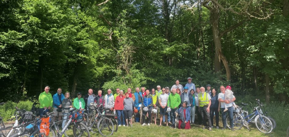 Mehrere Leute vor einem Wald stehend, links und rechts davon abgestellte Fahrräder