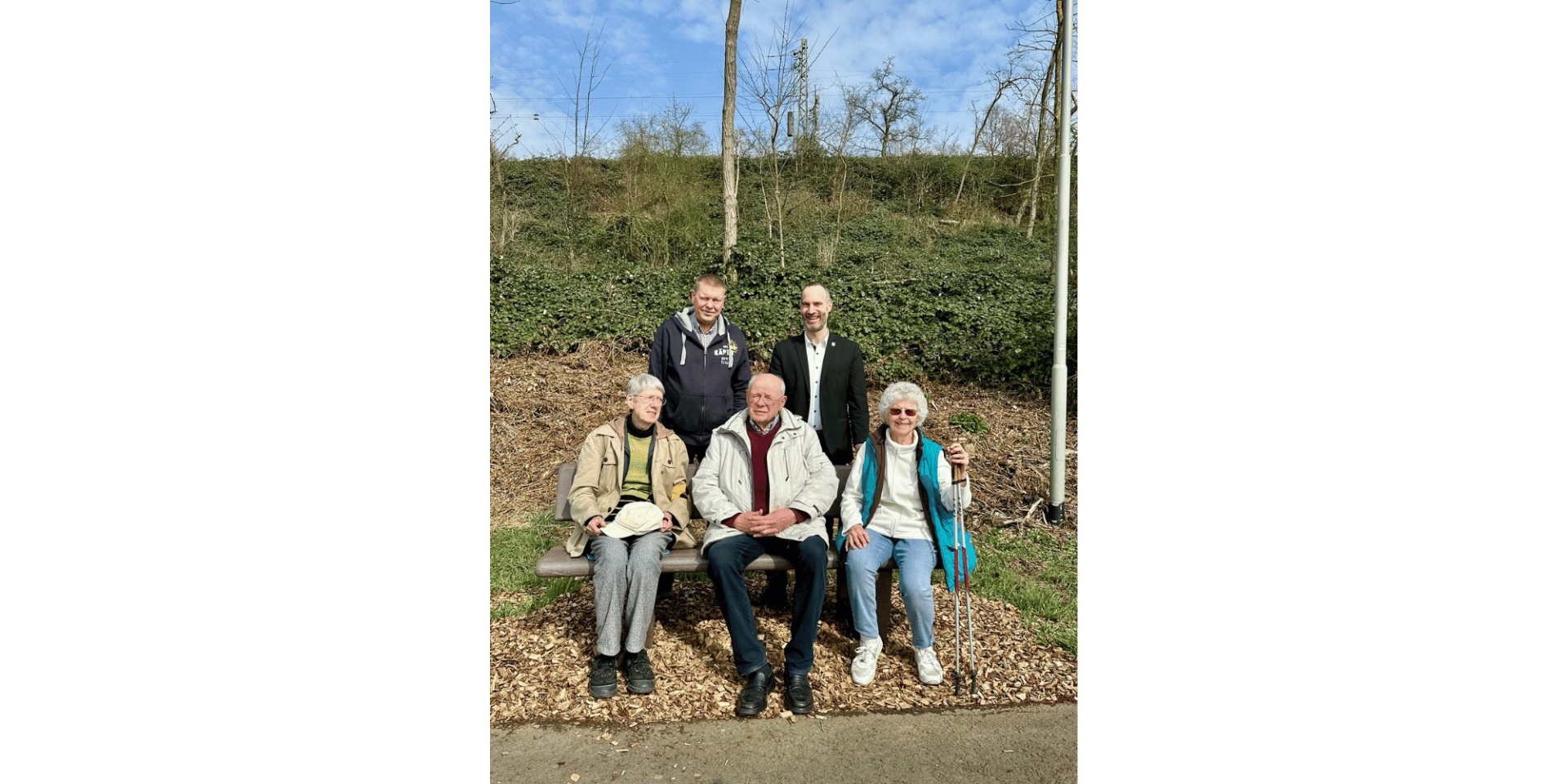 Drei Personen sitzend auf einer Ruhebank. Dahinter zwei Personen stehend