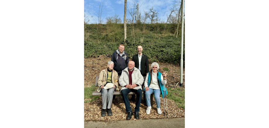 Drei Personen sitzend auf einer Ruhebank. Dahinter zwei Personen stehend