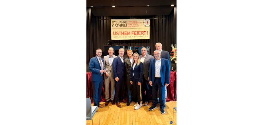 Mehrere Männer und eine Frau in dunklen Anzügen stehend auf einer Bühne