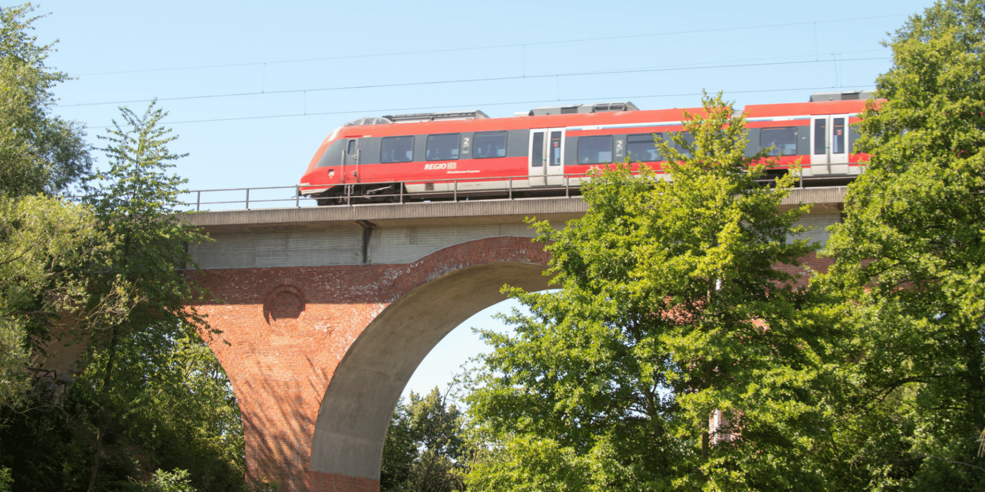 Eine rote Bahn fahrend über einen Viadukt umgeben von Bäumen